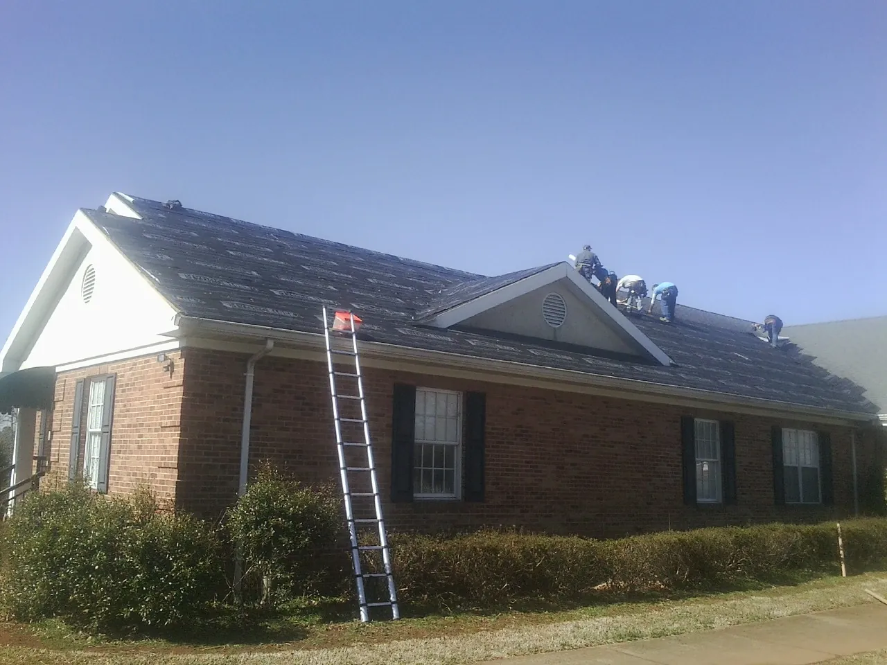 Crew tearing shingles off a brick ranch roof with a ladder set — Emergency Roof Repair work by our crew in Waynesfield