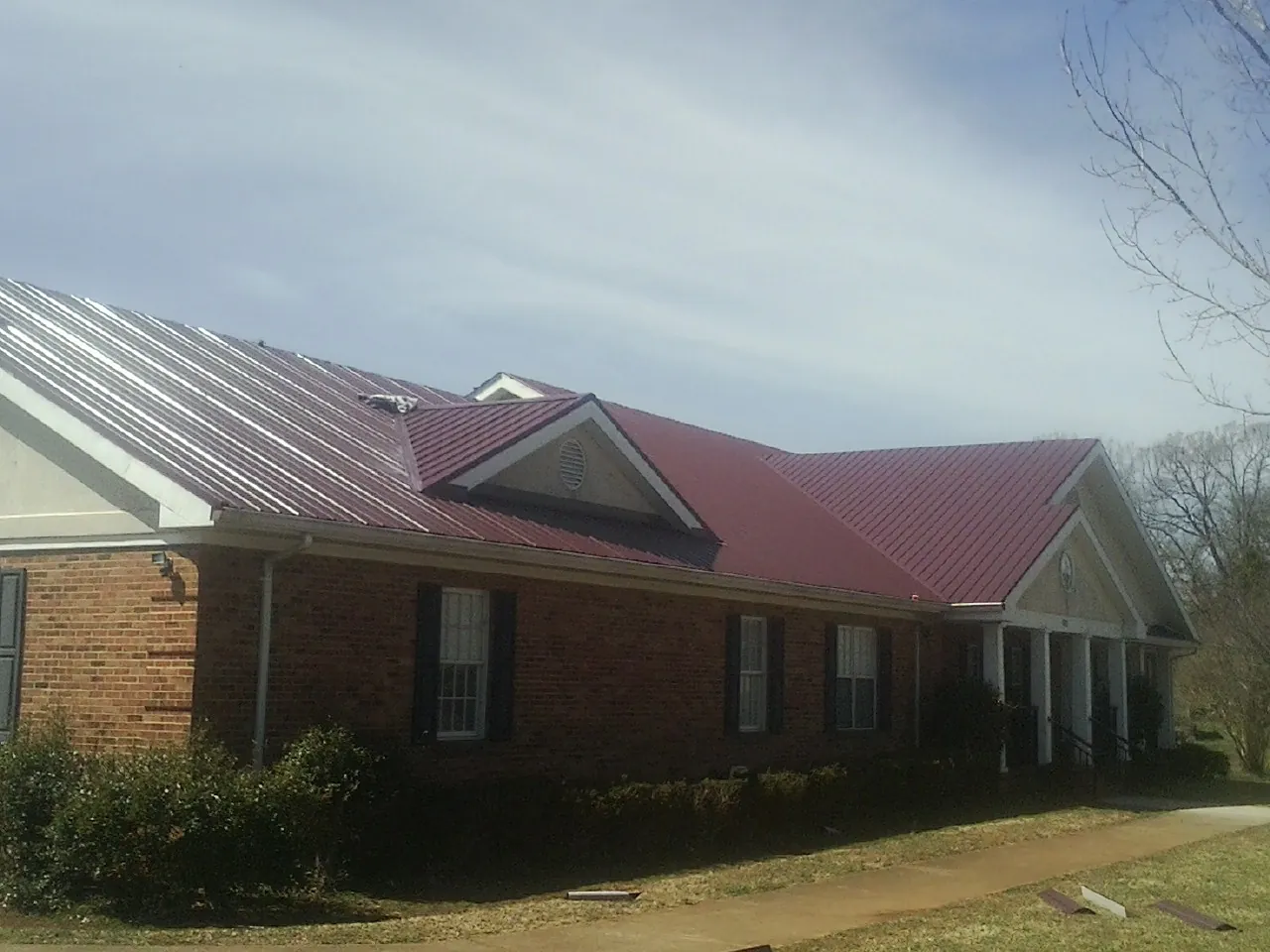 Red metal roof with gabled entries on a long brick building, from a Hail Damage Roof Repair job in Waynesfield