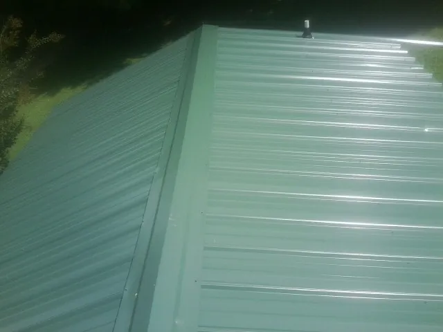 New green metal panels meeting at the ridge of a roof — Flat Roof Repair work by our crew in Waynesfield