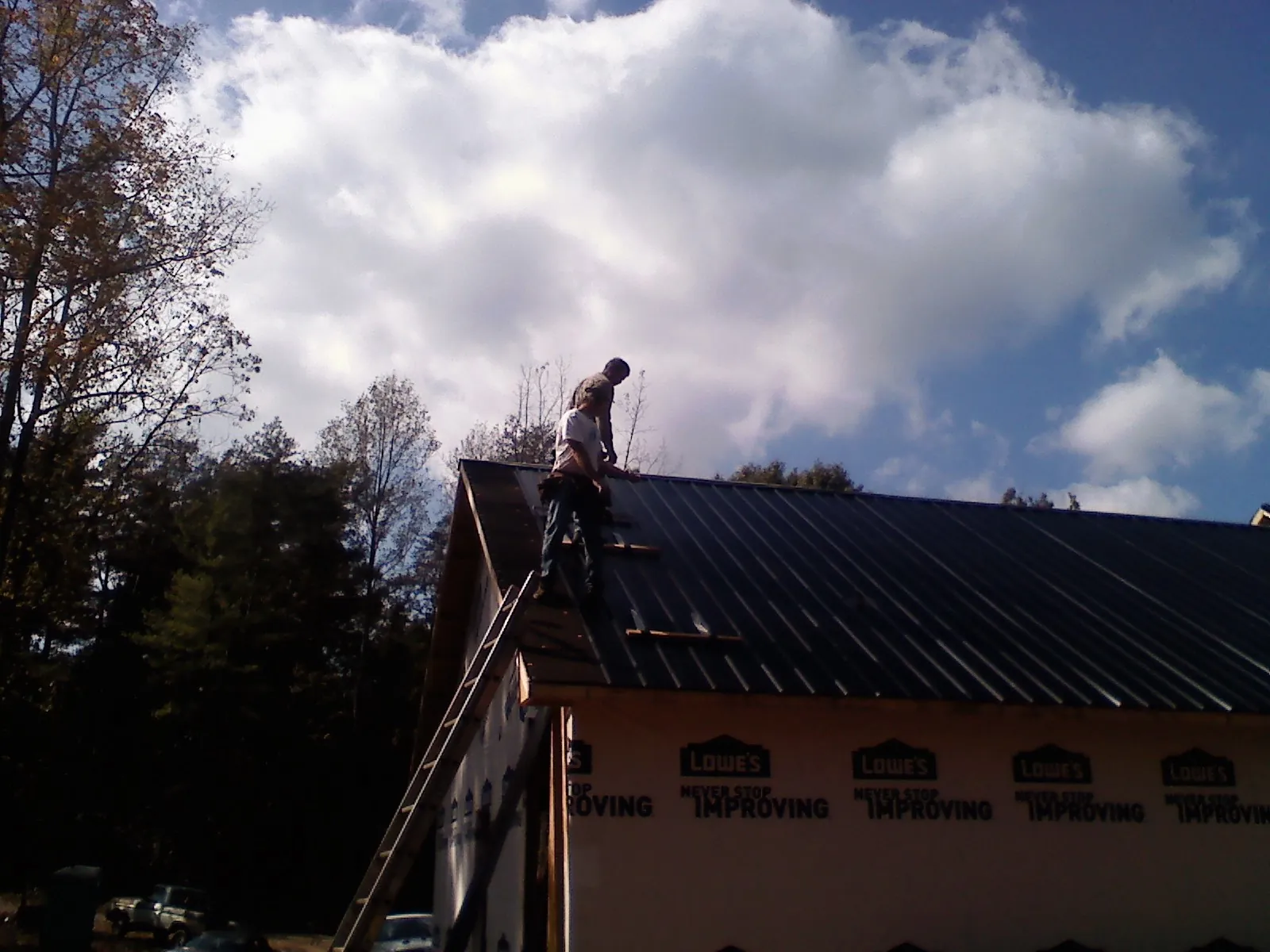 Roofer fastening dark metal panels high against a cloudy sky, from a Roof Inspection job in Waynesfield
