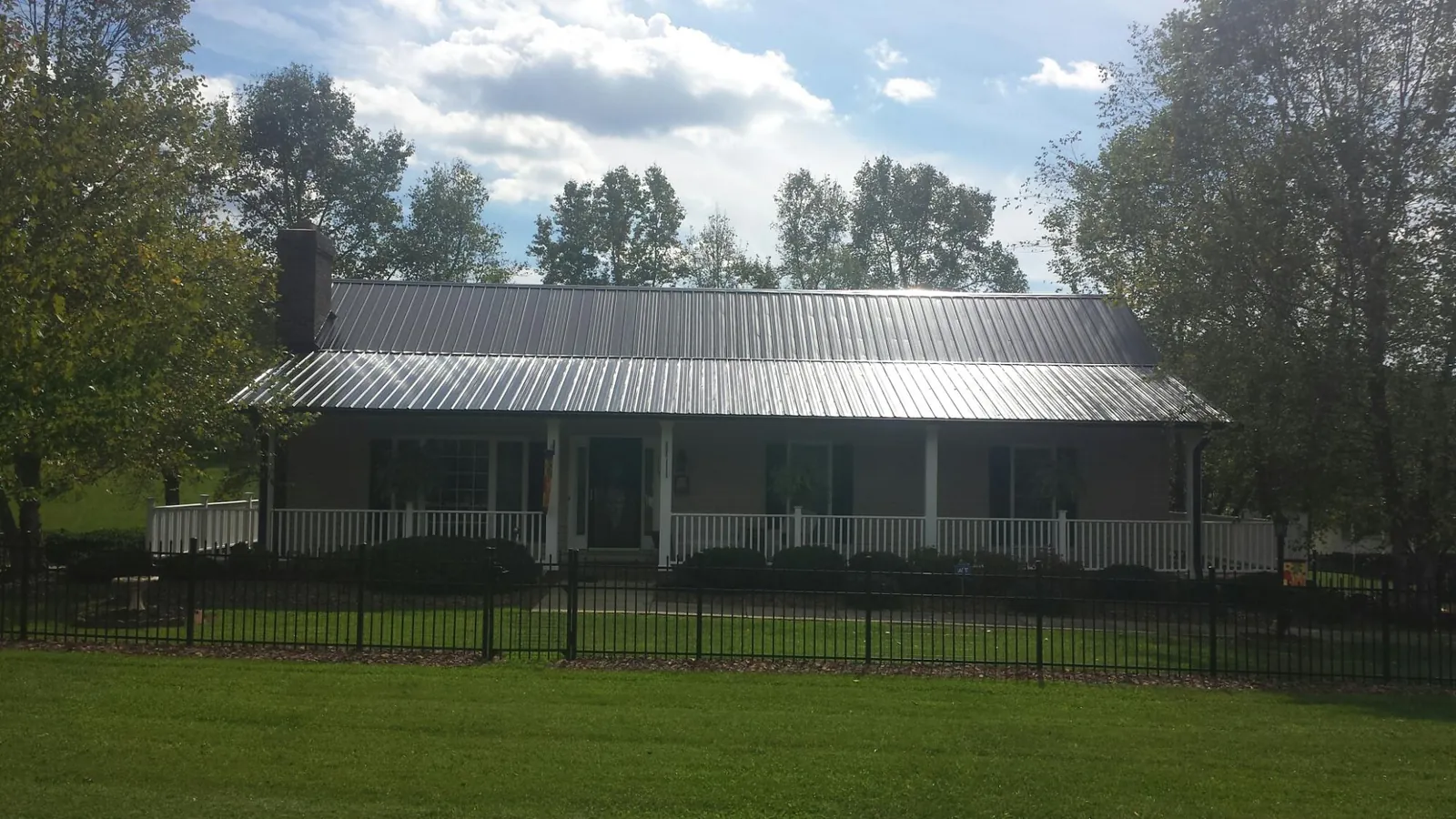 Gray metal roof on a brick ranch with a full width front porch — Gutter Guard Installation work by our crew in Waynesfield